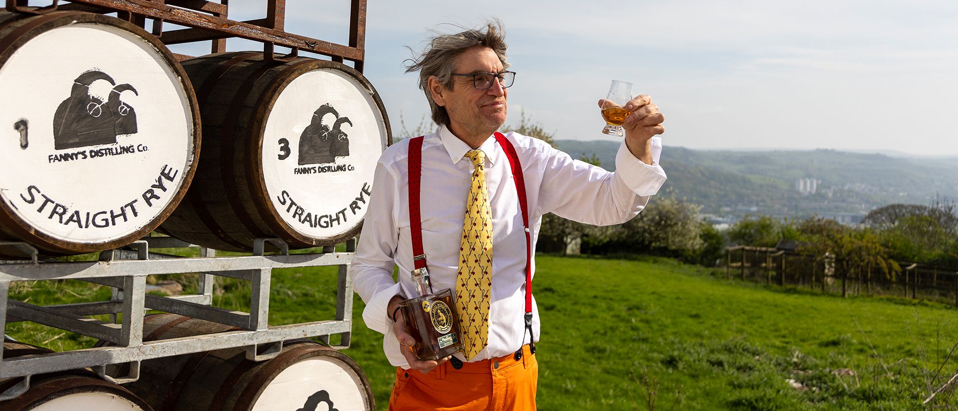 Marcus Lund raising a glass of rye beside Fanny's Distilling Co casks, high above the valley